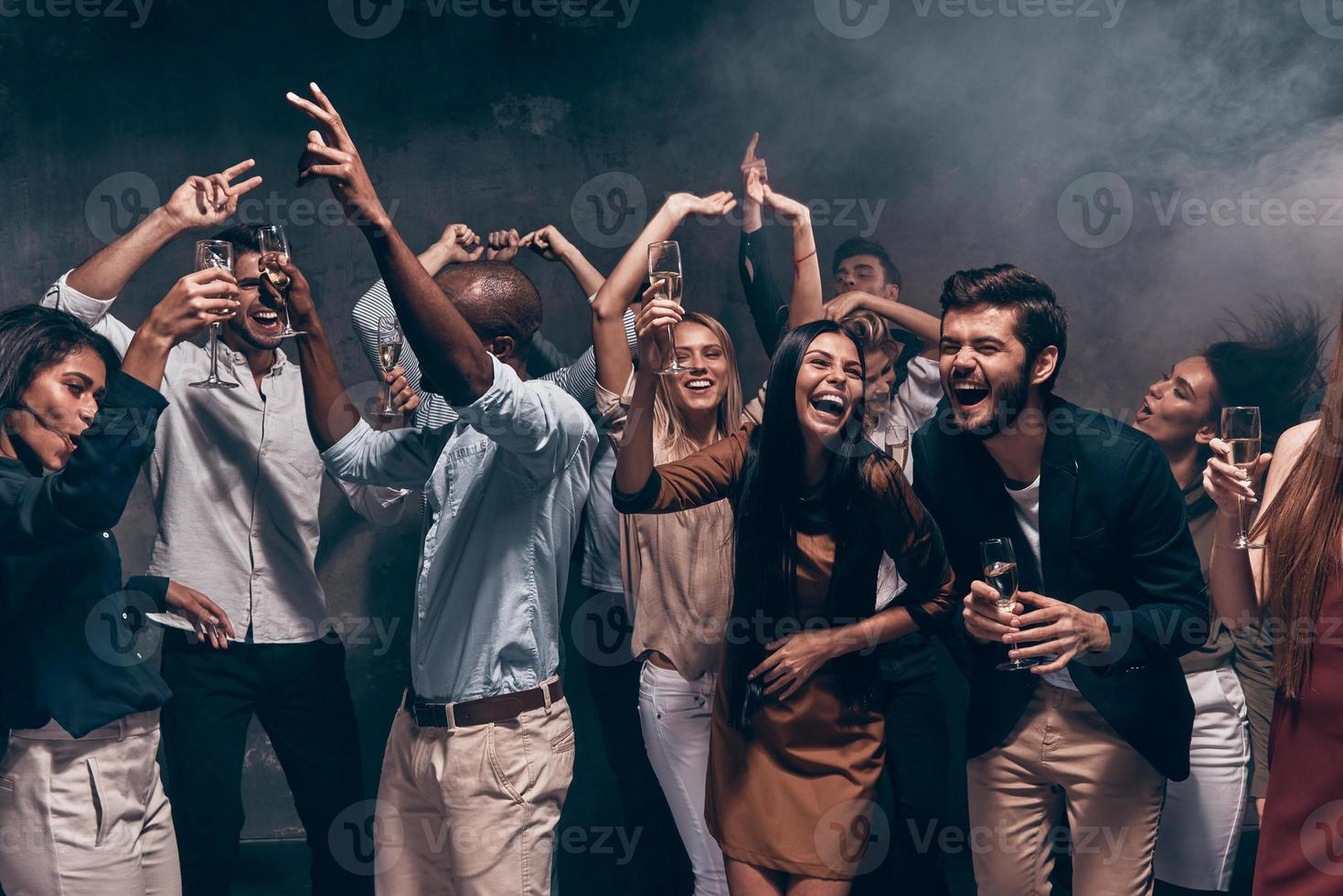 Genießen Sie eine tolle Party. Gruppe schöner junger Leute, die mit Champagnerflöten tanzen und glücklich aussehen foto