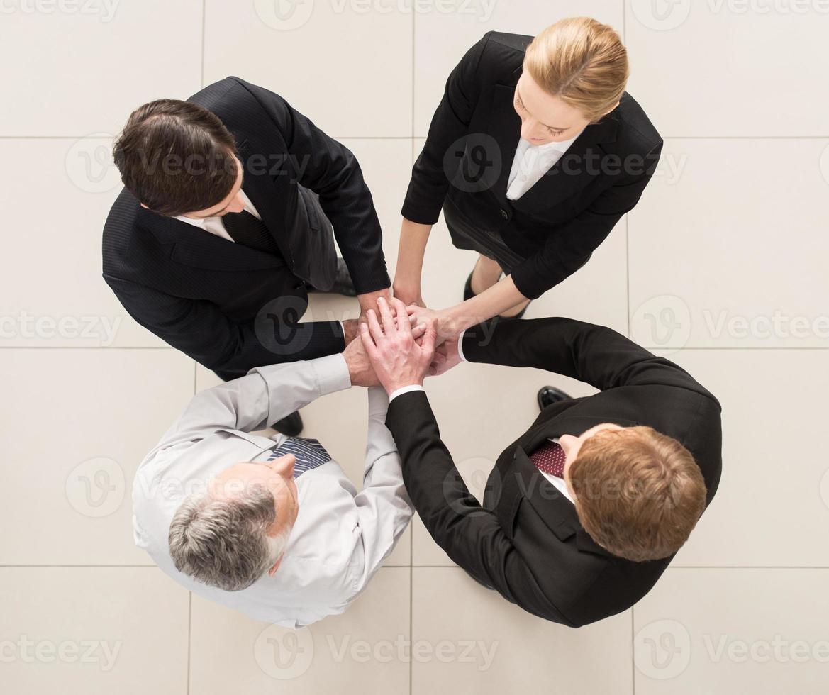 Wir sind Team-Draufsicht von vier Personen in formeller Kleidung, die nahe beieinander stehen und ihre Hände zusammenhalten foto