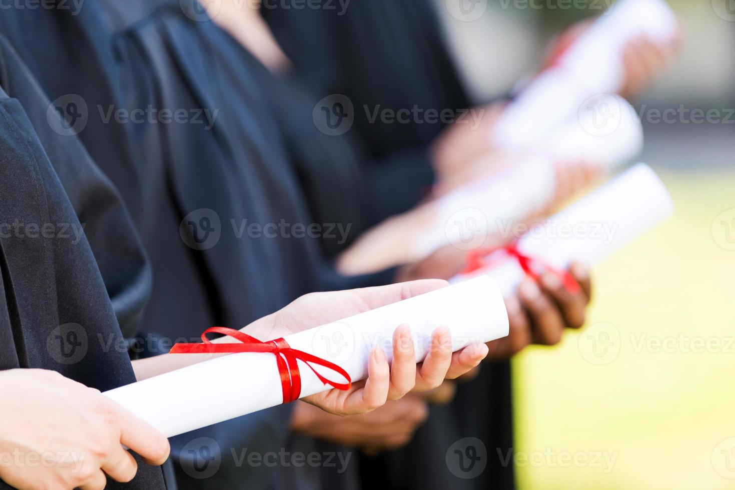 Absolventen mit Diplom. Nahaufnahme von vier Hochschulabsolventen, die in einer Reihe stehen und ihre Diplome halten foto