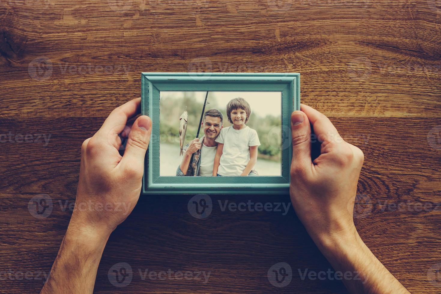 Mein Sohn ist mein Leben. Nahaufnahme von oben auf einen Mann, der ein Foto von sich und seinem Sohn hält, der über einem Holztisch fischt