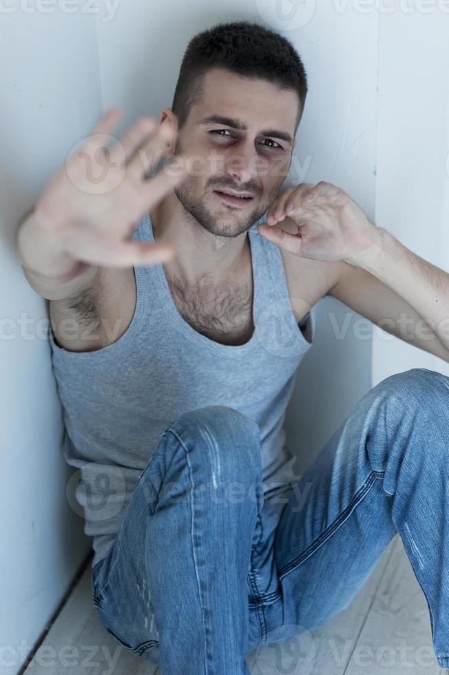 Bitte kein depressiver junger Mann, der auf dem Boden sitzt und die Hand in die Kamera streckt foto