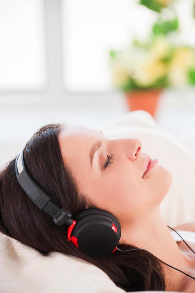Musik im Bett hören. Seitenansicht einer fröhlichen jungen Frau mit Kopfhörern, die MP3-Player hört und die Augen geschlossen hält foto