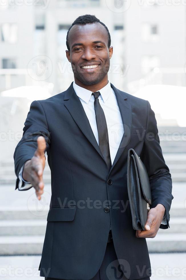 willkommen an bord hübscher junger afrikanischer mann im vollen anzug, der die hand zum schütteln ausstreckt, während er im freien steht foto