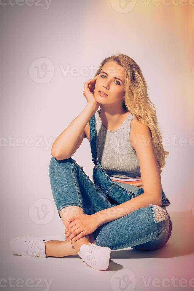 Liebe Denim. Studioaufnahme einer schönen jungen Frau in Jeans, die insgesamt in die Kamera schaut, während sie auf dem Boden sitzt foto