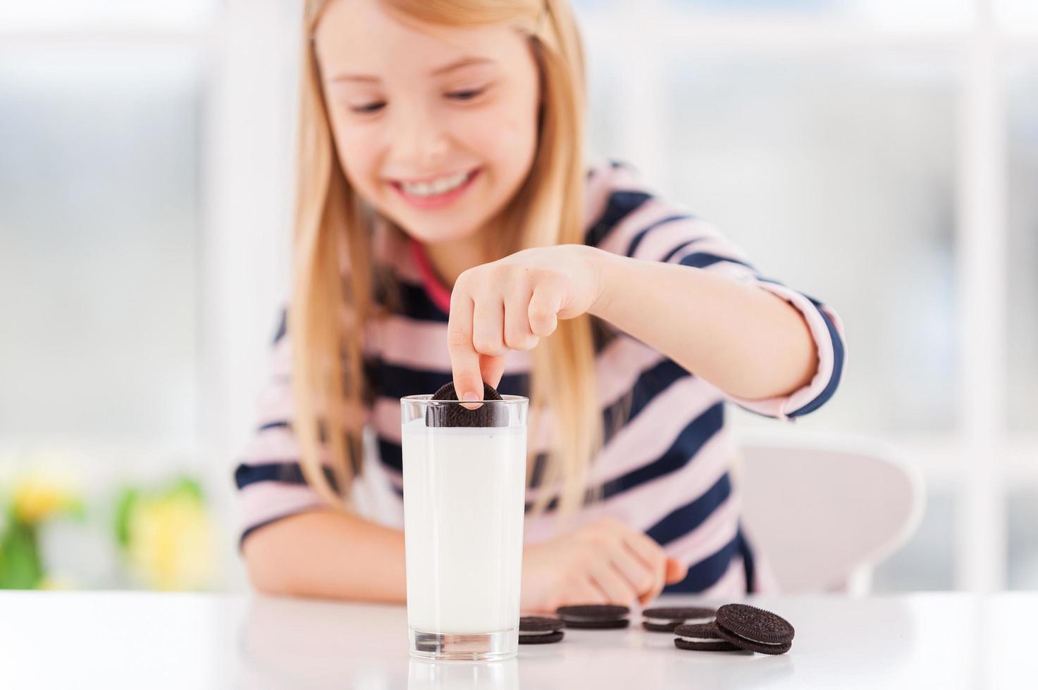 einen Keks eintauchen. süßes kleines Mädchen, das Plätzchen in Milch taucht und lächelt foto