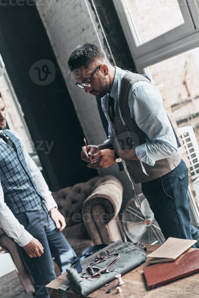 sorgfältig notieren. zwei junge modische Männer, die eine Diskussion führen, während sie in der Werkstatt stehen foto