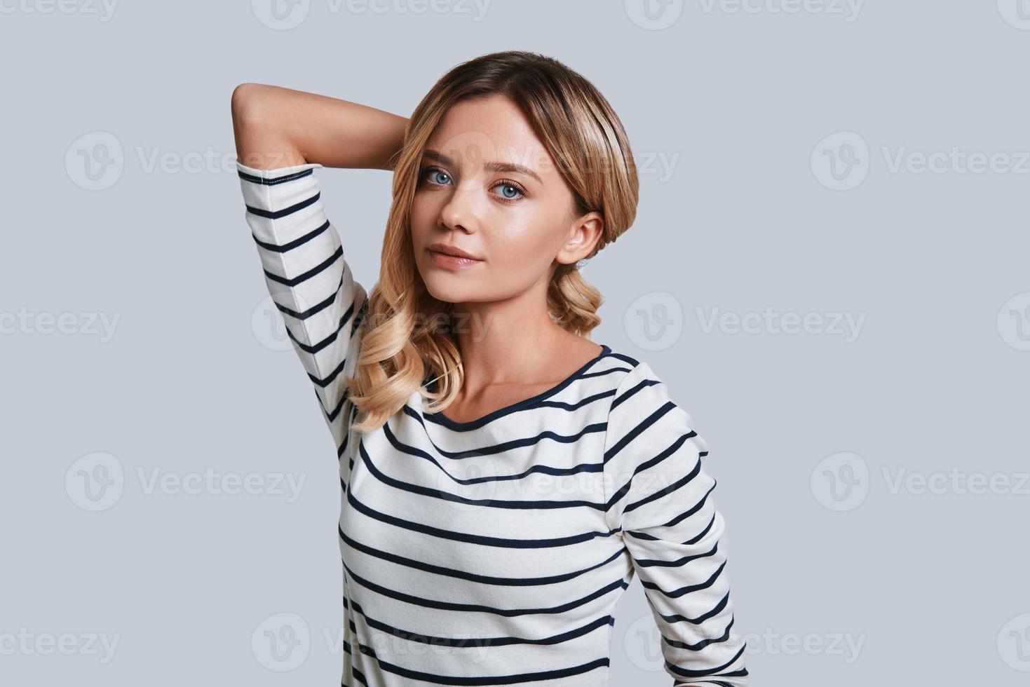 wahre weibliche Schönheit. attraktive junge Frau, die Kamera beim Stehen gegen grauen Hintergrund lächelt und betrachtet foto