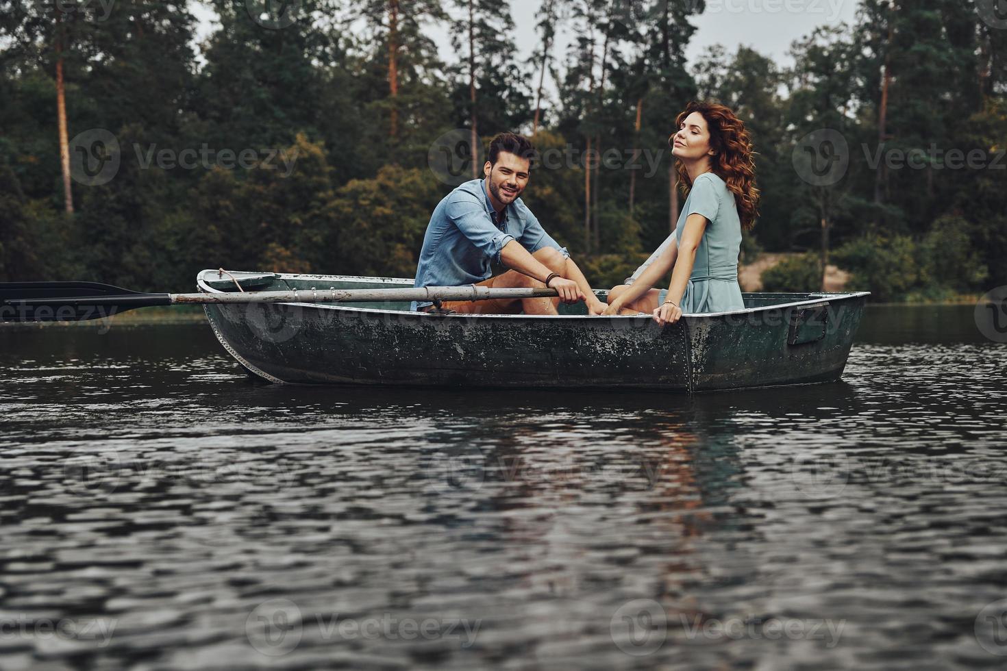 glücklich, einander zu haben. Schönes junges Paar, das ein romantisches Date genießt und beim Rudern eines Bootes lächelt foto