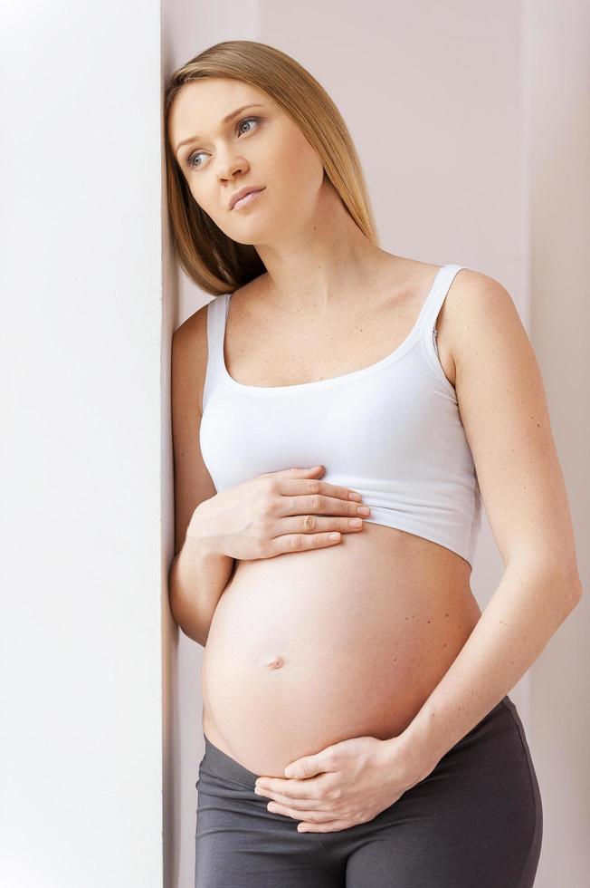 erwartendes Baby. nachdenkliche schwangere Frau, die sich an die Wand lehnt und wegschaut foto
