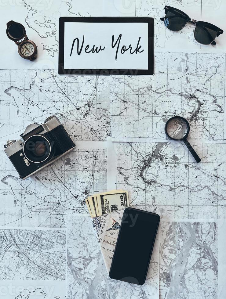 Halten Sie eine Reise mit hohem Winkel von Sonnenbrille, Fotokamera, Kompass, Lupe, Smartphone, Reisepass und Währung auf der Karte foto