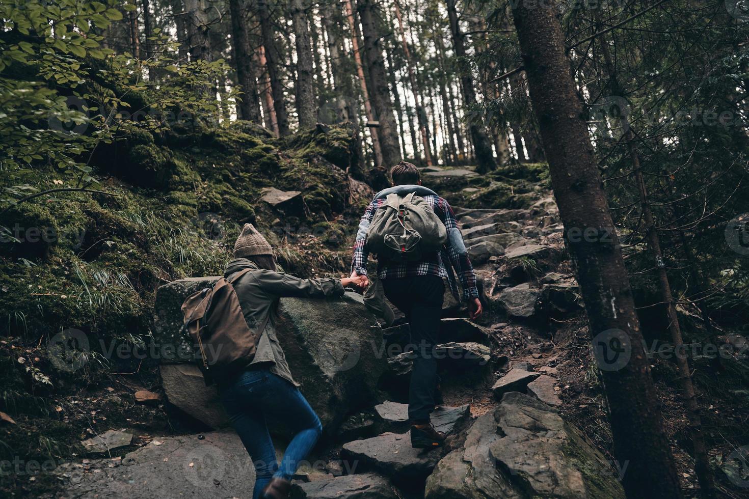 einander helfen. Rückansicht des jungen Paares Händchen haltend beim gemeinsamen Wandern im Wald foto