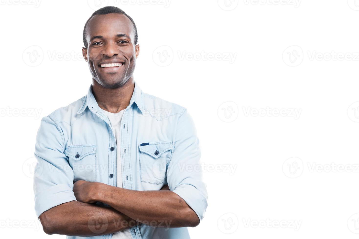 erfolgreicher und glücklicher Mann. hübscher junger schwarzer Mann, der die Arme verschränkt hält und in die Kamera lächelt, während er vor weißem Hintergrund steht foto