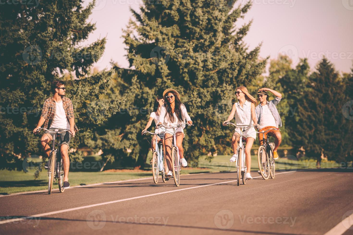 toller tag zum radeln. Gruppe junger Leute, die Fahrräder entlang einer Straße fahren und glücklich aussehen foto