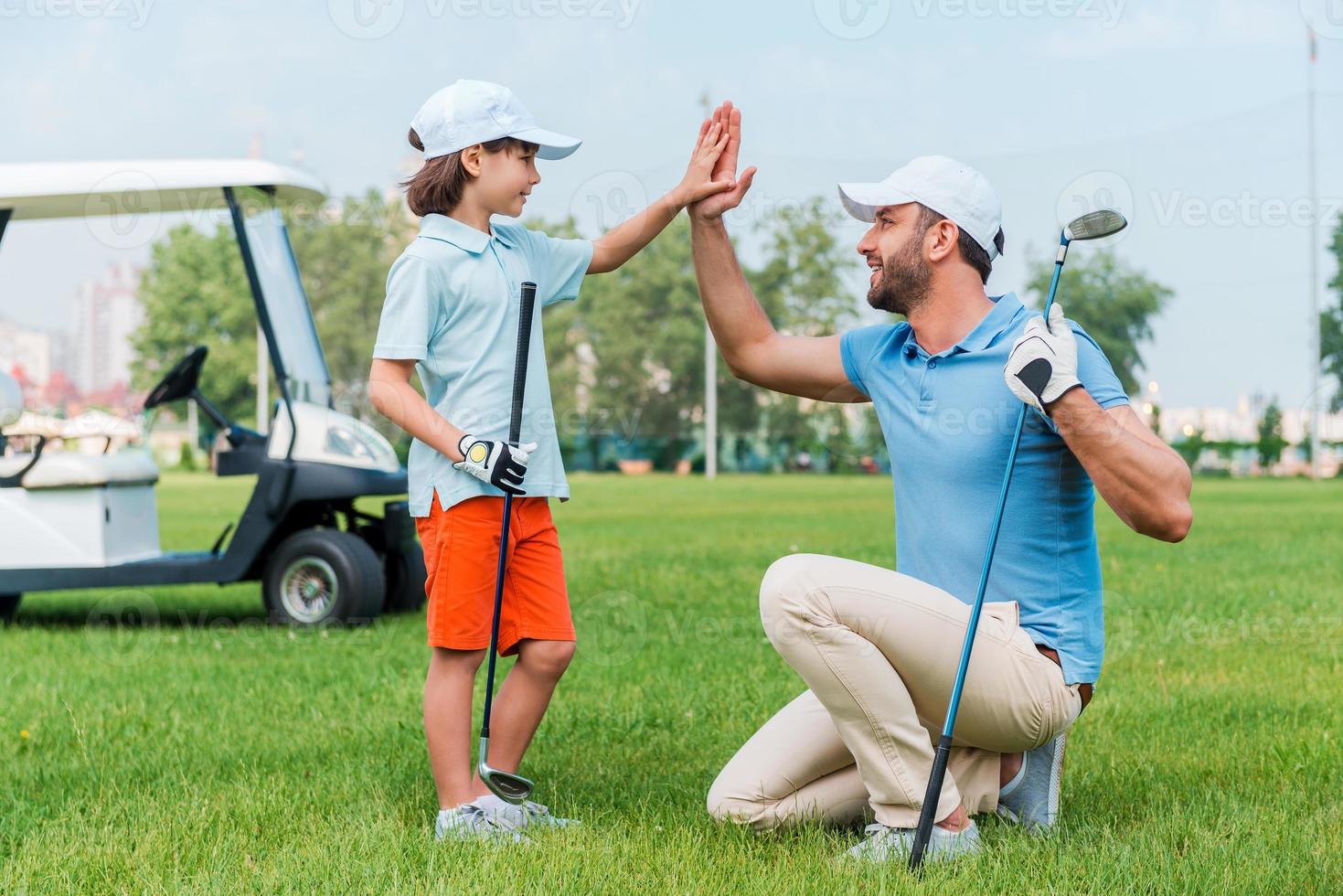 mein kleiner gewinner fröhlicher junger mann und sein sohn klatschen sich gegenseitig ab, während sie auf dem golfplatz stehen foto