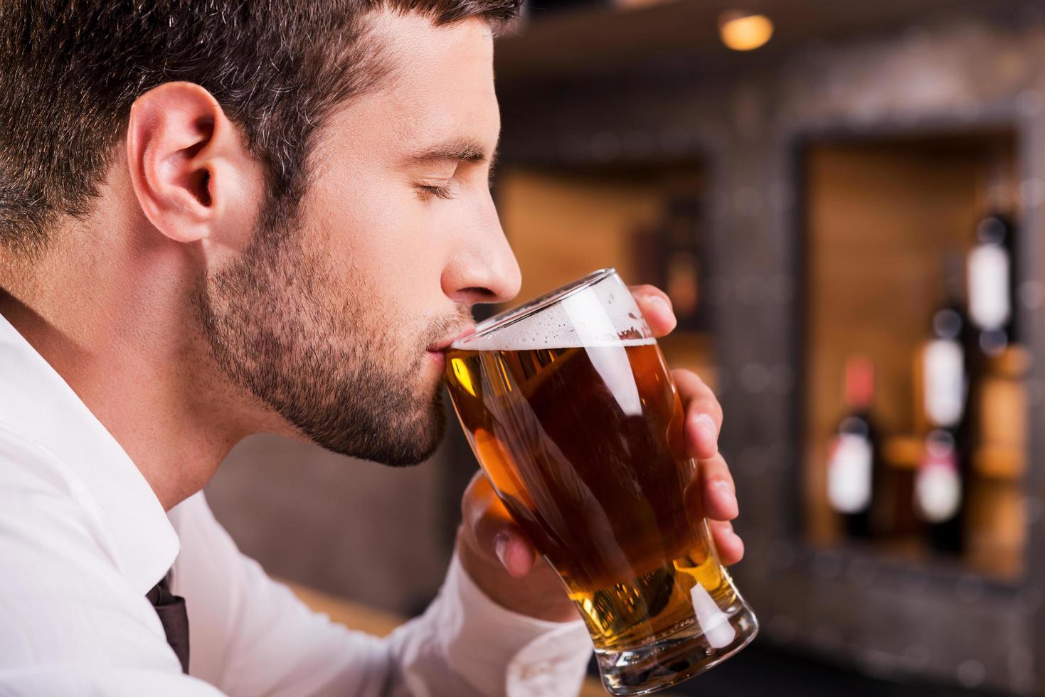 Mann trinkt Bier. Seitenansicht eines hübschen jungen Mannes, der Bier trinkt, während er an der Bartheke sitzt foto