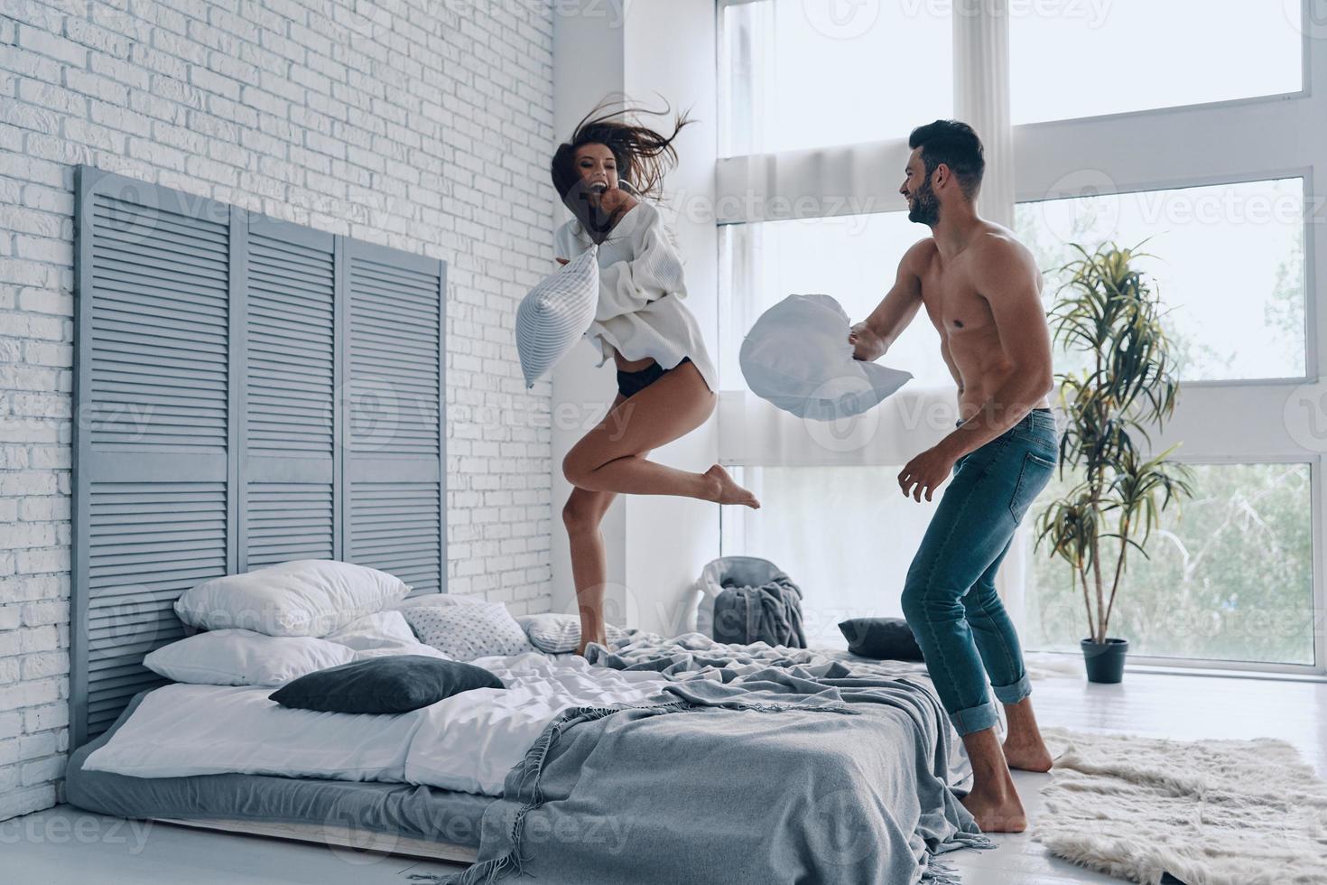 lustige Zeit. in voller länge von glücklichen jungen paaren, die eine lustige kissenschlacht haben, während sie sorglose zeit im schlafzimmer verbringen foto