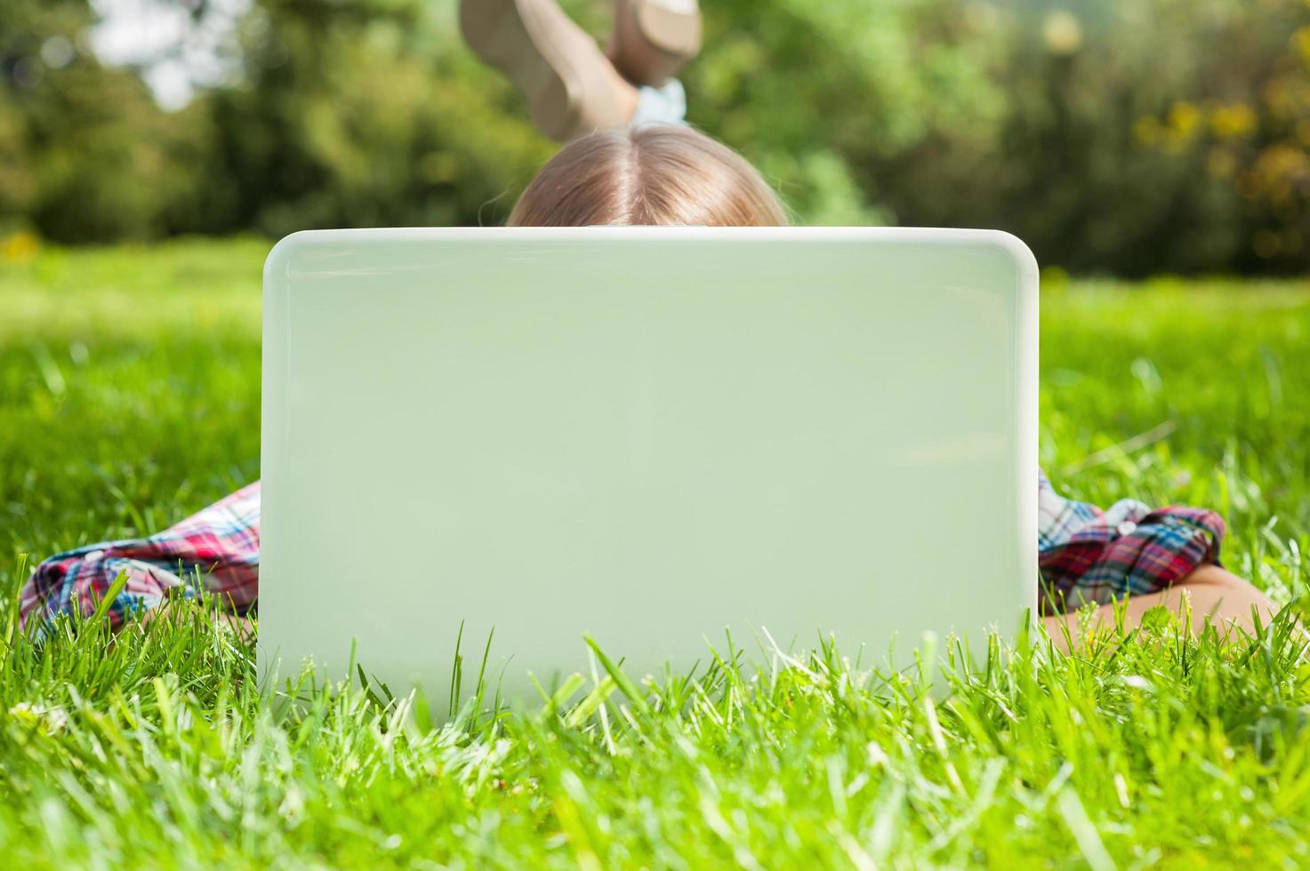 Computer und frische Luft. Frau versteckt Gesicht hinter Laptop-Monitor, während sie auf dem Gras im Park liegt foto