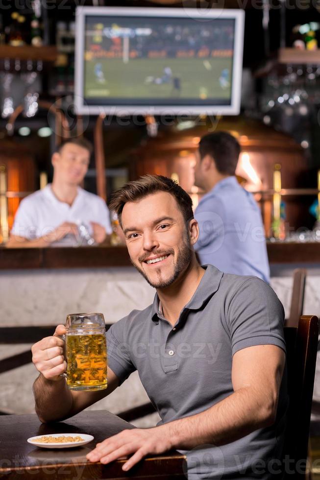 Mann in der Bierkneipe. hübscher junger Mann, der einen Bierkrug hält und lächelt, während er in der Bar sitzt foto