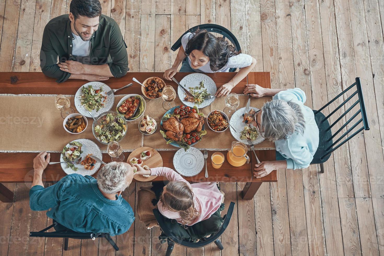 Draufsicht einer Familie mit mehreren Generationen, die beim gemeinsamen Abendessen kommuniziert und lächelt foto