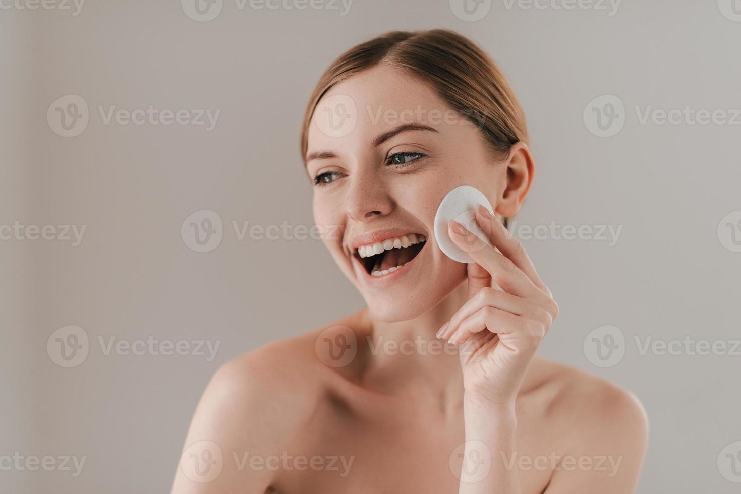 bringt Frische auf ihre Haut. Studioporträt einer attraktiven Frau, die ihre Haut mit einem Wattepad reinigt, während sie vor dem Hintergrund steht foto