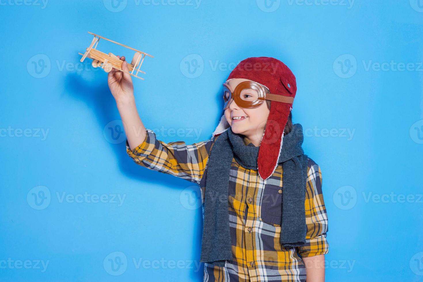 auf den Wellen meiner Phantasie. glücklicher kleiner Junge im Helm, der mit Spielzeugflugzeug spielt, während er vor blauem Hintergrund steht foto