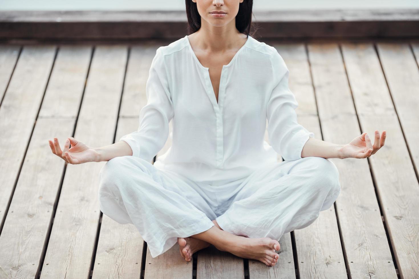 in Frieden und Gleichgewicht mit der Welt. Zugeschnittenes Bild einer schönen jungen Frau in weißer Kleidung, die im Lotussitz sitzt und im Freien meditiert foto