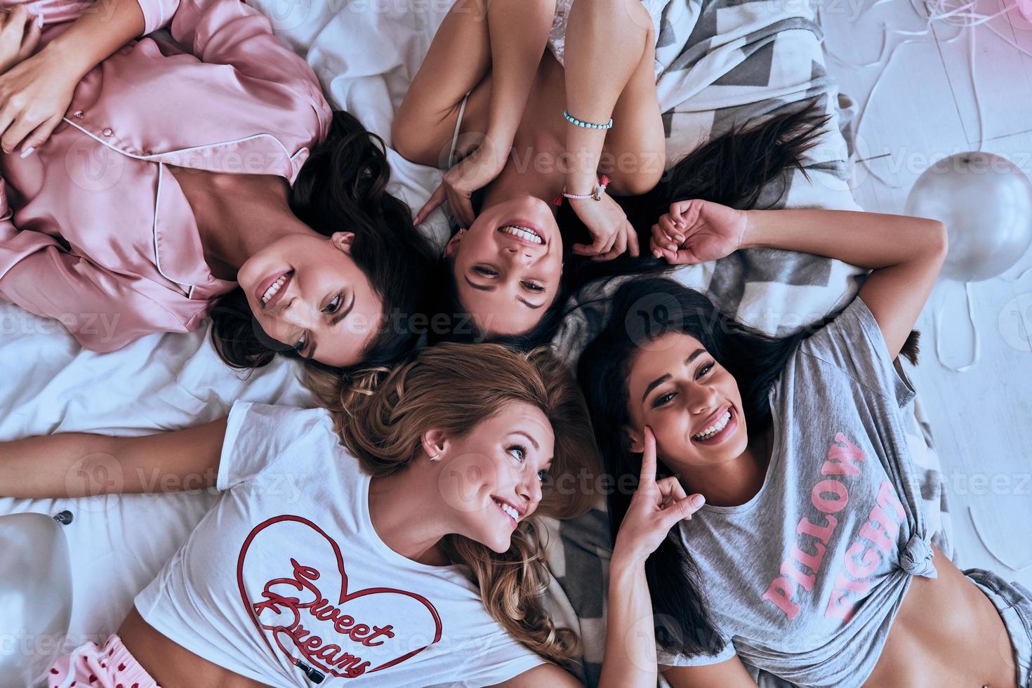 wirklich lustig. Draufsicht von vier verspielten jungen Frauen, die lächeln, während sie zu Hause auf dem Bett liegen foto