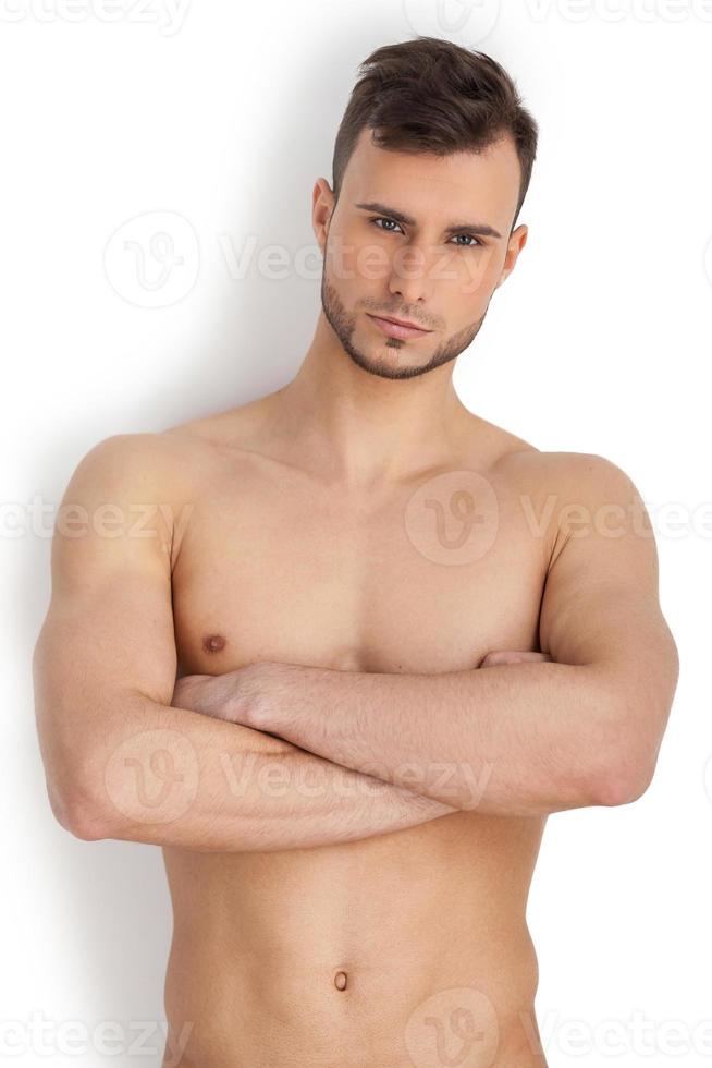 Porträt der Männlichkeit. Nachdenklicher junger muskulöser Mann, der in die Kamera schaut und die Arme verschränkt hält, während er isoliert auf weißem Hintergrund steht foto