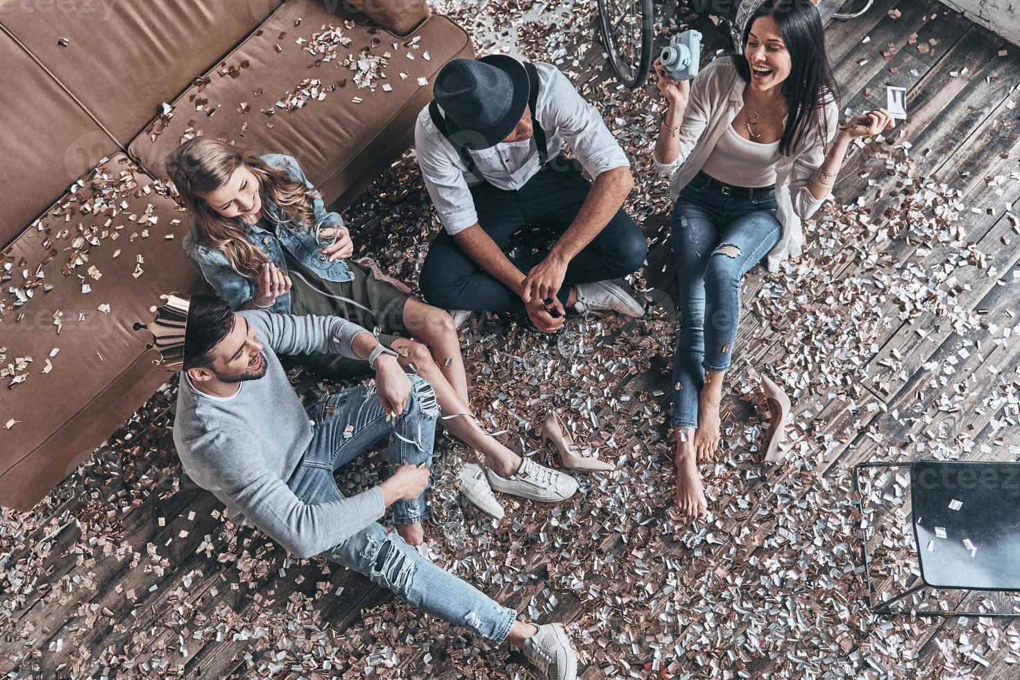 zusammen verrückt werden. Draufsicht auf moderne junge Menschen, die sich ausruhen, während sie mit Konfetti auf dem Boden sitzen foto