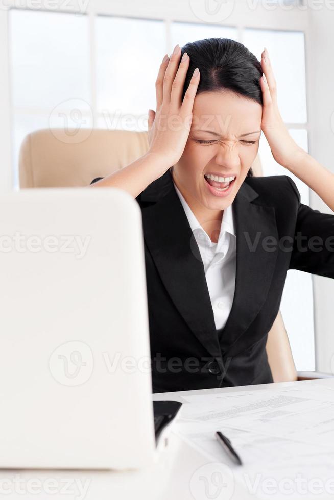 Emotionaler Stress. Junge Geschäftsfrau, die den Kopf in den Händen hält und schreit, während sie an ihrem Arbeitsplatz sitzt foto