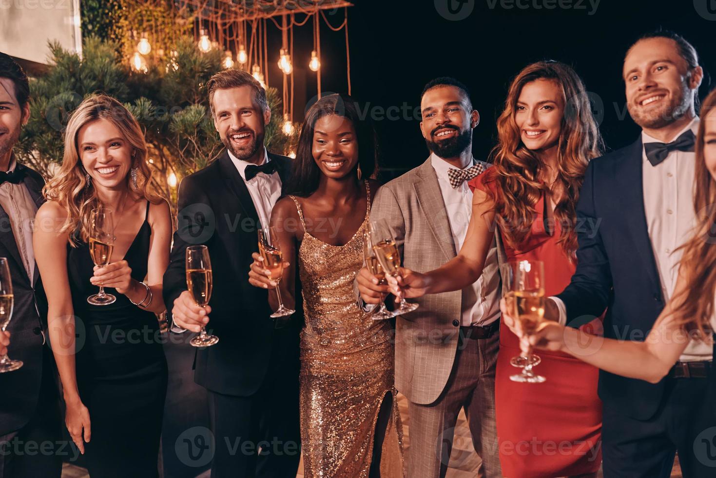 Gruppe von Menschen in formeller Kleidung, die mit Champagner anstoßen und lächeln, während sie Zeit auf einer Luxusparty verbringen foto