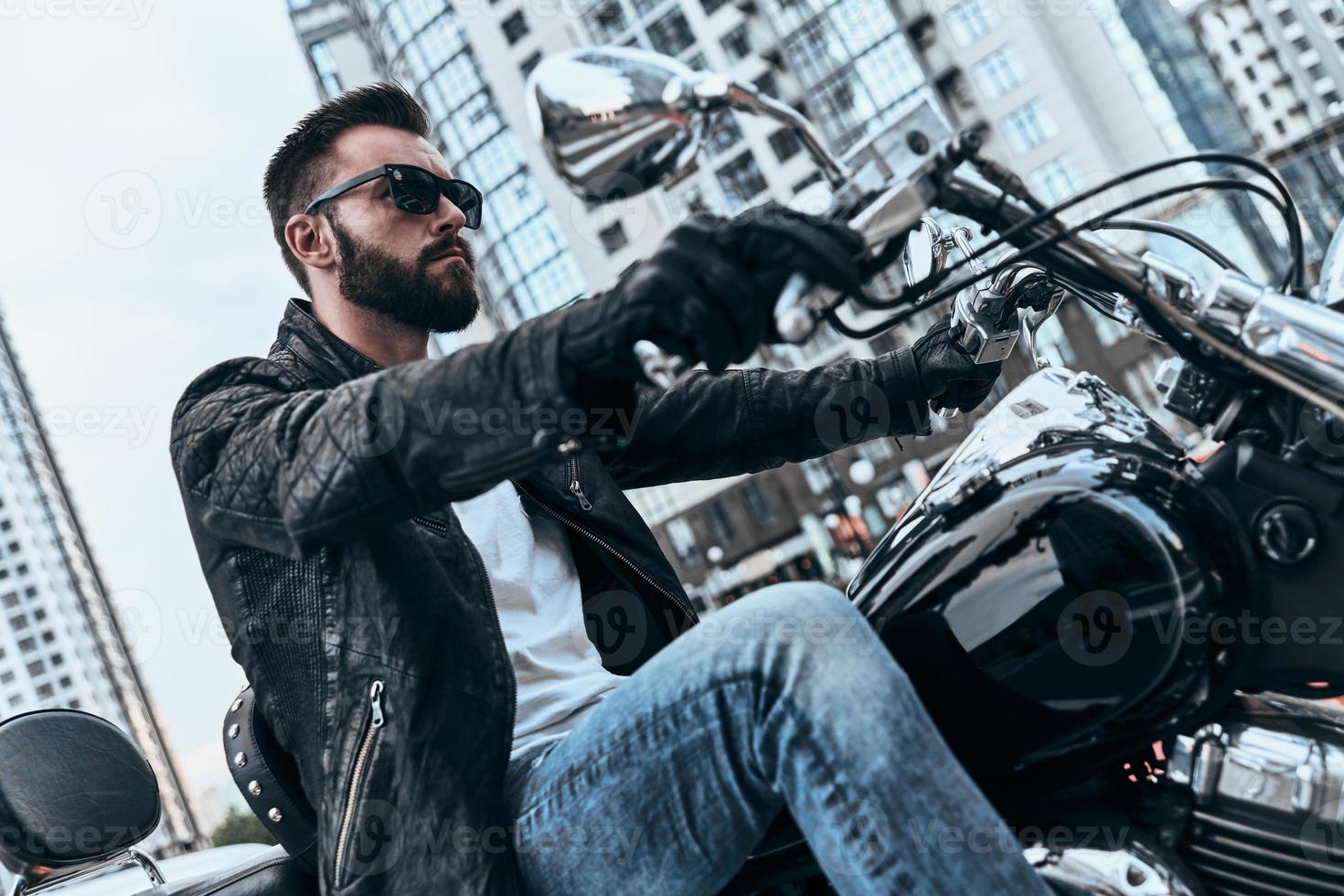 Herzensbrecher. hübscher junger Mann in Lederjacke und Sonnenbrille, der Motorrad fährt, während er Zeit im Freien verbringt foto