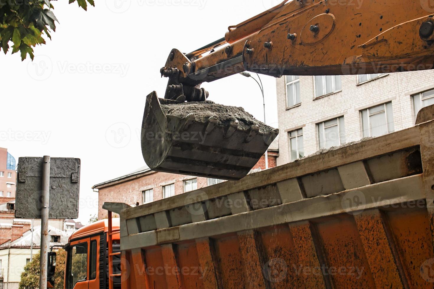 Straßenarbeiten auf der Stadtstraße. die baggerschaufel sammelt das alte pflaster und lädt es in einen muldenkipper foto