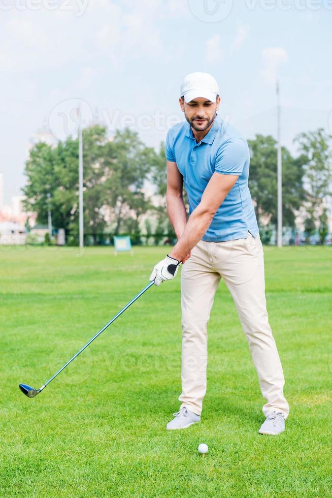 letzten Schlag ins Ziel. Selbstbewusster junger Mann, der Golf spielt, während er auf dem Golfplatz steht foto