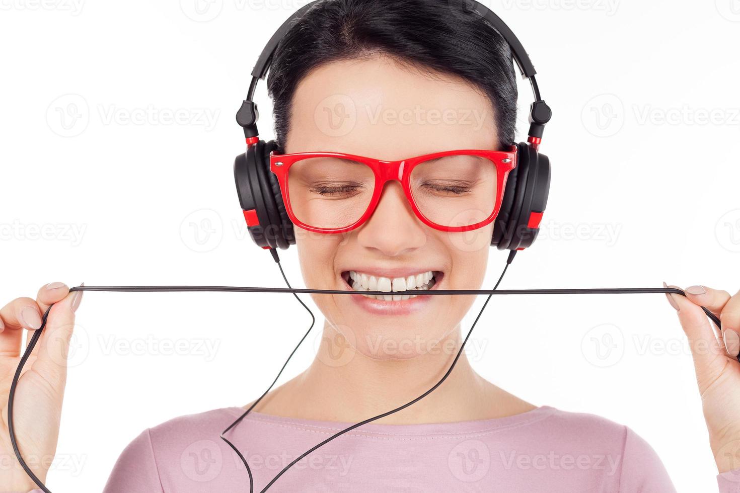 es ist ihr lieblingslied. Schöne junge Frau mit roter Brille und Kopfhörern, die Musik hört und die Augen geschlossen hält, während sie isoliert auf Weiß steht foto