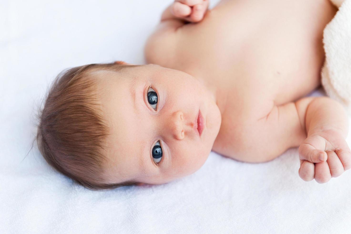 süßes Baby. Blick von oben auf das kleine Baby, das im Bett liegt und in die Kamera schaut foto