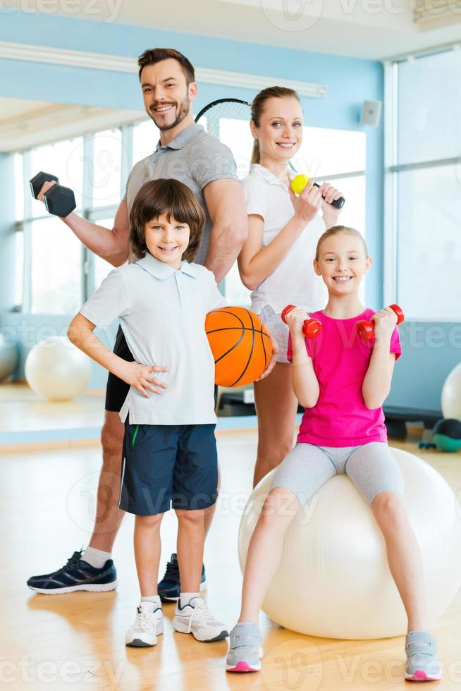 sportliche Familie. glückliche familie, die verschiedene sportgeräte hält, während sie im fitnessclub nahe beieinander stehen foto