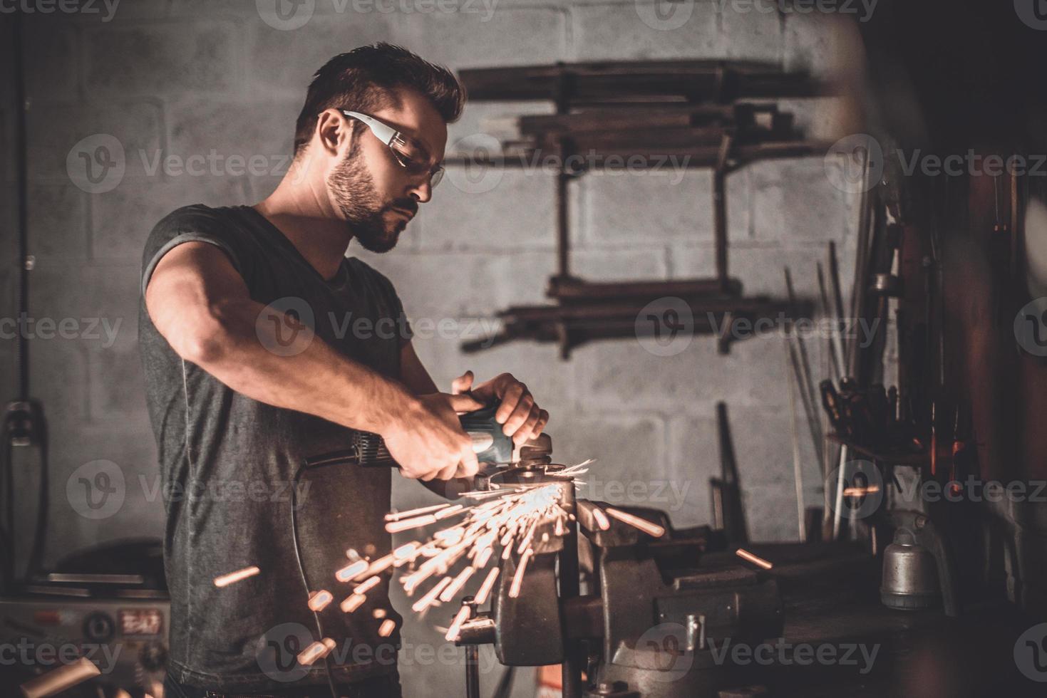 Mann bei der Arbeit. Selbstbewusster junger Mann, der in der Werkstatt mit Funken schleift foto