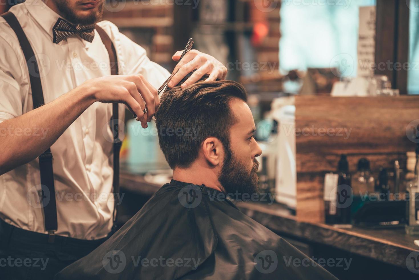 Perfekter Schnitt von hinten nach vorne. Nahaufnahme eines jungen bärtigen Mannes, der vom Friseur im Friseursalon die Haare geschnitten bekommt foto