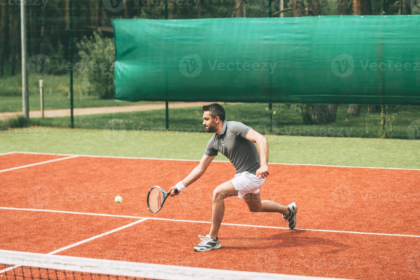 Mann spielt Tennis. Selbstbewusster junger Mann in Sportkleidung, der Tennis auf dem Tennisplatz spielt foto