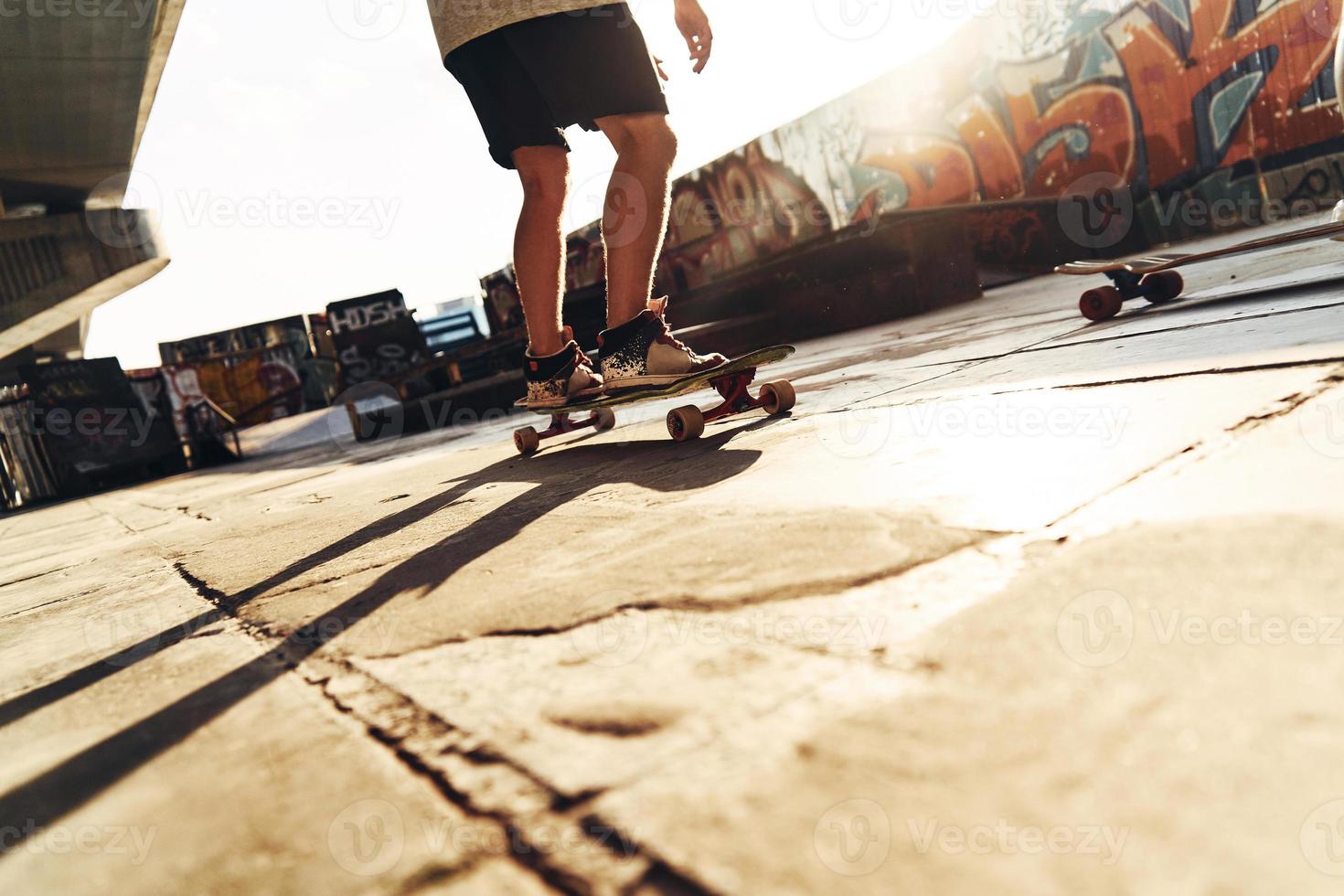 Skater unterwegs. Nahaufnahme eines modernen jungen Mannes, der Skateboard fährt, während er draußen im Skatepark rumhängt foto