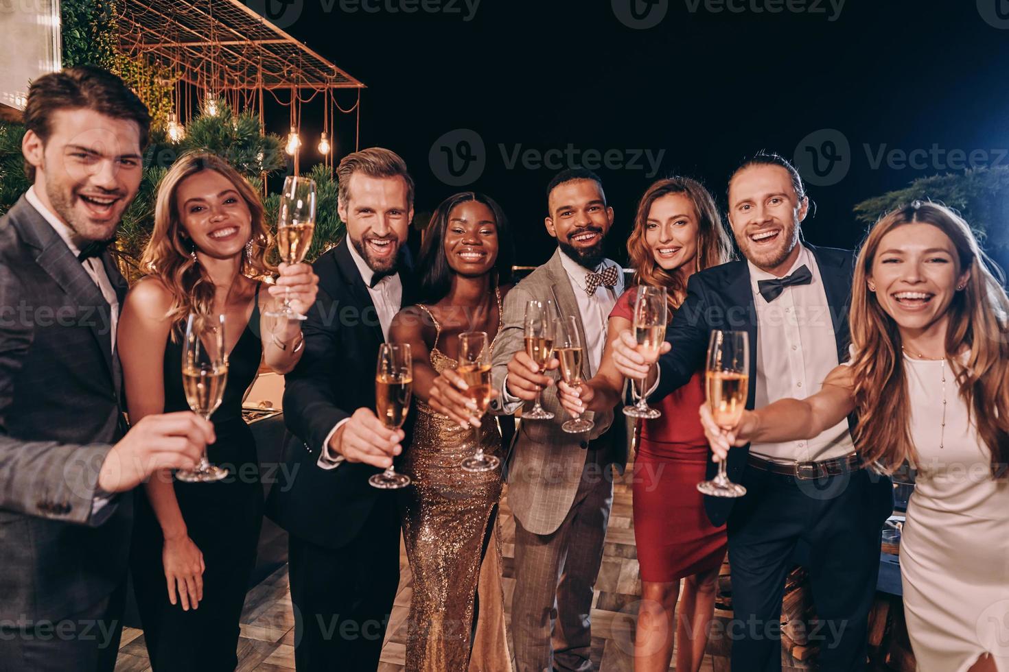 Gruppe von Menschen in formeller Kleidung, die mit Champagner anstoßen und lächeln, während sie Zeit auf einer Luxusparty verbringen foto