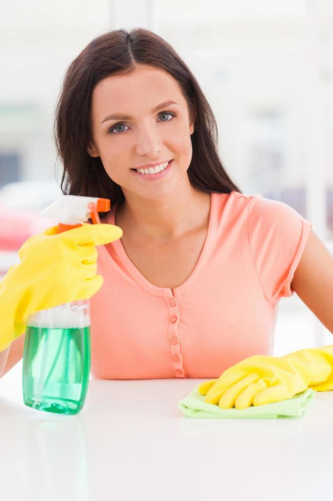 Hausfrau bei der Arbeit. junge schöne Frau in gelben Handschuhen, die einen Lappen und eine Sprühflasche hält, während sie in die Kamera lächelt foto