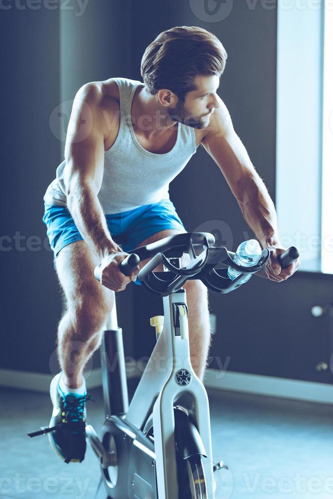 Fahrt zum Erfolg. junger gutaussehender mann in sportbekleidung radfahren im fitnessstudio foto