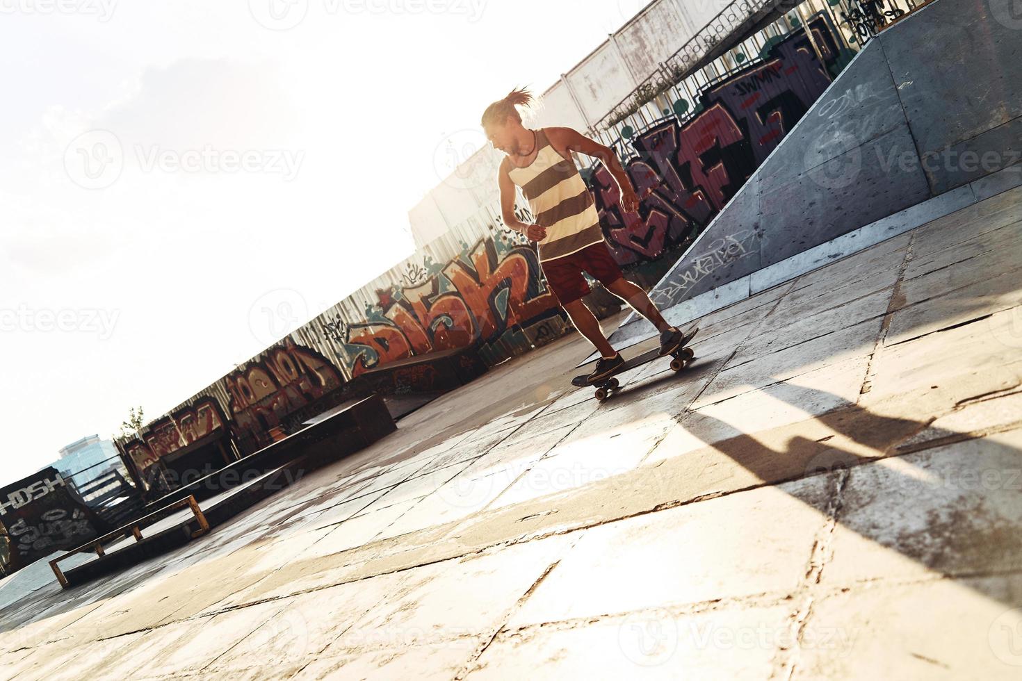 voller Länge des Skateboardens eines jungen Mannes, während er draußen im Skatepark rumhängt foto