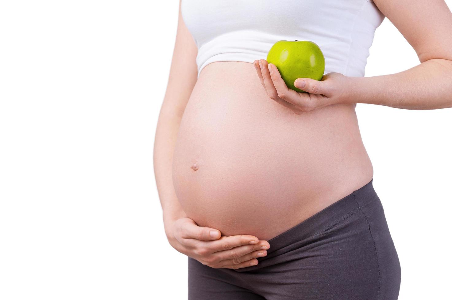 nur gesundes essen. Zugeschnittenes Bild einer schwangeren Frau, die einen grünen Apfel hält, während sie isoliert auf Weiß steht foto