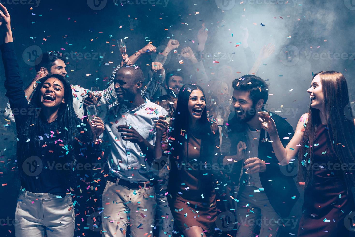 zusammen eine tolle Party genießen. gruppe schöner junger leute, die buntes konfetti werfen und glücklich aussehen foto