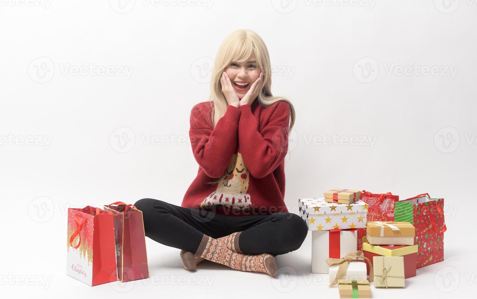 Porträt einer glücklichen kaukasischen jungen Frau in Weihnachtspullover mit Geschenkbox und Einkaufstüten auf weißem Hintergrund foto