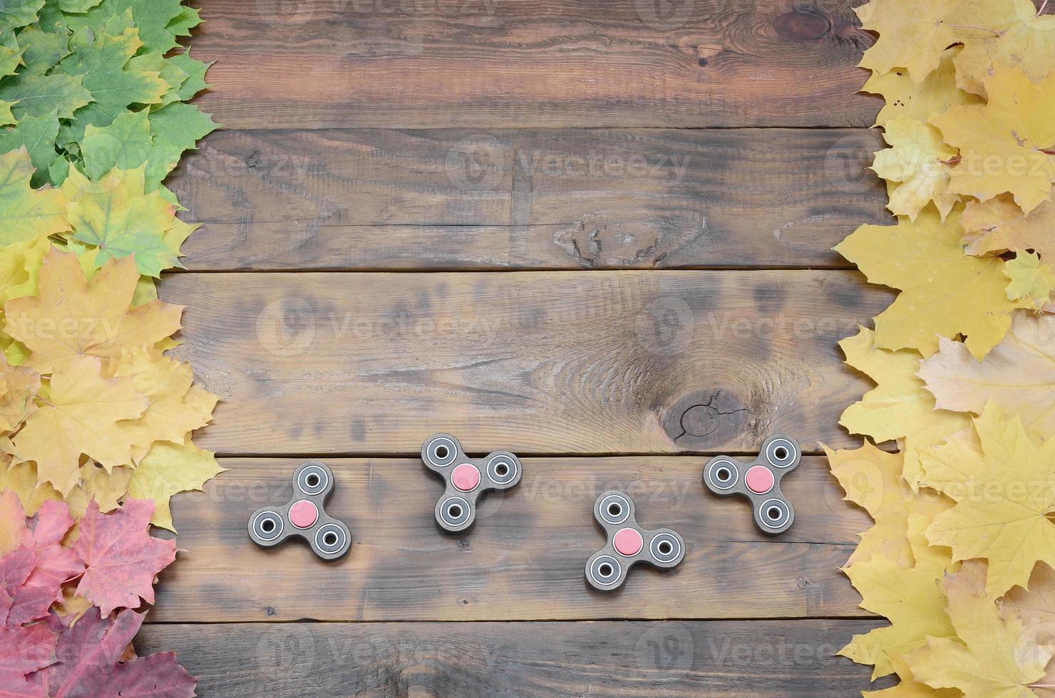 Mehrere Spinner unter den vielen vergilbten gefallenen Herbstblättern auf der Hintergrundoberfläche von natürlichen Holzbrettern von dunkelbrauner Farbe foto