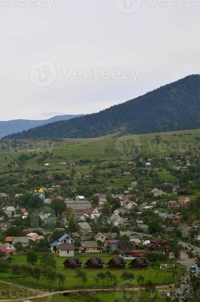 eine schöne aussicht auf das dorf mezhgorye, karpatengebiet. Viele Wohngebäude, umgeben von hohen Waldbergen und einem langen Fluss foto